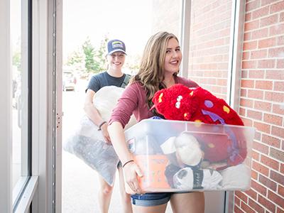 Two students carry in their items on Move-In day.